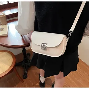 Detail of cream crossbody bag with woven texture and silver geometric buckle on a table