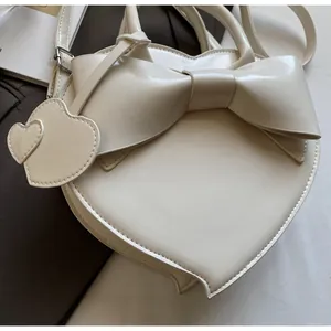 Detail of a creamy white heart-shaped shoulder bag with a large bow and double heart charm
