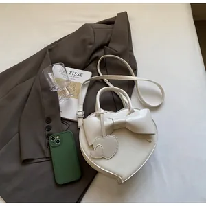 Detail of cream heart-shaped crossbody bag with oversized bow and twin heart charms