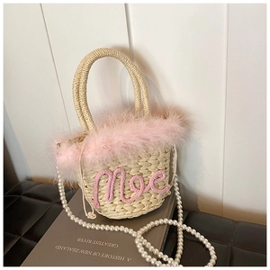 Close-up of woven straw bucket bag with pink feathers, text embroidery and pearl strap