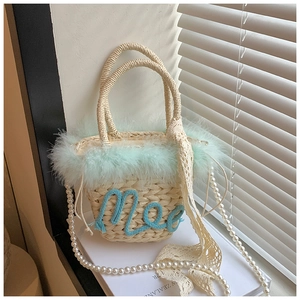 Detail of woven straw handbag featuring light green feather trim and a pearl chain strap