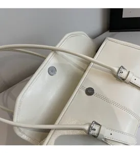 Detail view of cream leather shoulder bag showing silver magnetic closure and glossy texture
