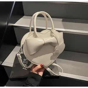 Detail of cream heart-shaped crossbody bag with bow decoration and detachable strap