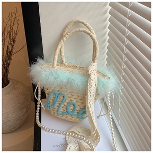Close-up of woven straw handbag with green feather trim and pearl shoulder strap