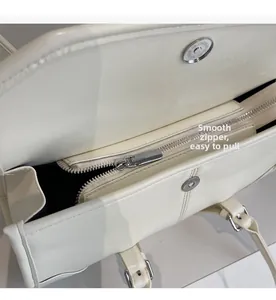 Close-up of smooth silver zipper and magnetic buckle on off-white faux leather tote bag