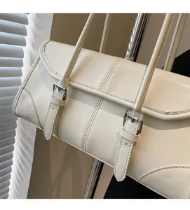 Close-up of cream leather underarm bag featuring dual buckle flap and stitched details