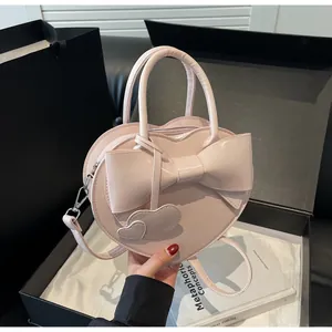 Pink heart-shaped handbag with decorative bow and charm held against a gift box background