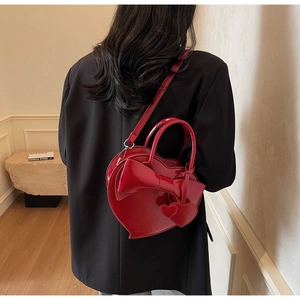 Dettaglio della borsa a cuore in pelle verniciata rossa con fiocco indossata da modella