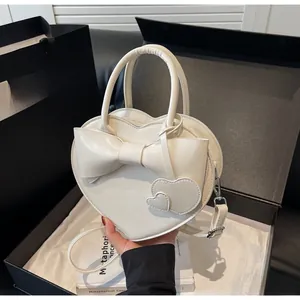 Detail of white heart-shaped handbag featuring a 3D bow and elegant heart charms