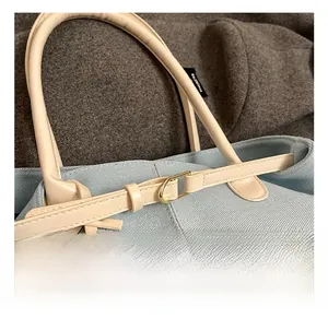 Detalle de bolso denim azul claro con asa de cuero crema y herraje de anillo D dorado