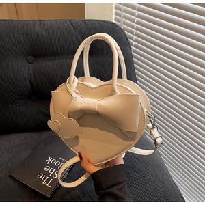 Détail d'un sac beige en forme de cœur avec grand nœud et finitions argentées sur canapé