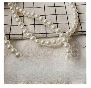 Detailed close-up of glossy white pearls on an elegant handmade woven evening bag strap
