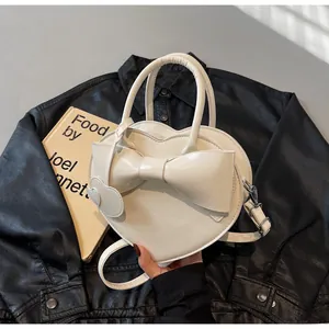 Detail of white heart-shaped handbag featuring a large bow and shiny PU leather finish
