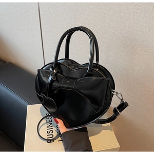 Détail d'un sac à main noir en forme de cœur avec un grand nœud brillant