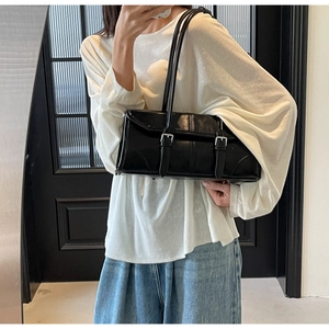 Detail of glossy black leather shoulder bag with metallic buckles on white outfit