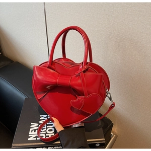 Détail d'un sac coeur en cuir verni rouge avec nœud et pendentifs décoratifs
