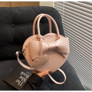 Detail of pink heart-shaped handbag with large bow and twin heart charms on a sofa