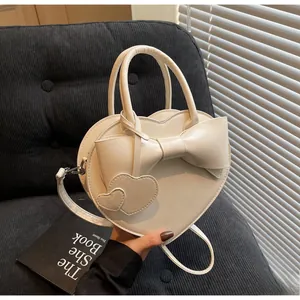 Detail of cream heart-shaped bag with large bow and double heart charms held by a model