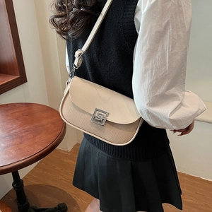Chic beige leather and woven saddle bag with silver buckle worn by a model in a cafe