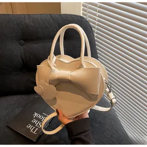 Detail of cream white heart-shaped bag with large bow and heart charms on a sofa