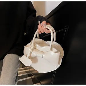 Detail of a heart-shaped cream handbag with a large bow and glossy finish for women