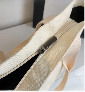 Close-up of smooth metal zipper and premium stitching on cream canvas tote bag detail