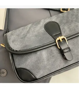Détail du sac à bandoulière en denim gris avec bordure en cuir noir et boucle dorée