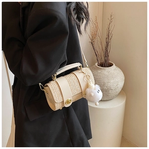Detail of beige cylindrical bag featuring woven texture and a gold ring handle