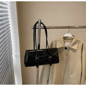 Detail of a black vintage baguette bag with buckle straps hanging on a beige trench coat