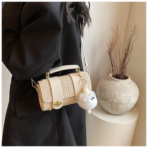 Detail of beige woven crossbody bag featuring a plush doll charm and gold twist-lock