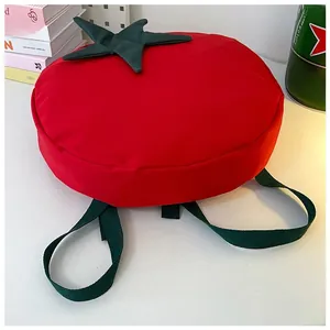 Detail of red tomato shaped backpack with green leaf accents on a white desktop