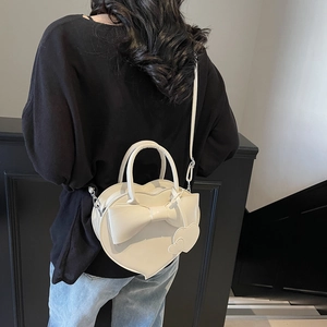 Sac bandoulière blanc chic en forme de cœur avec nœud porté à l'épaule par un mannequin