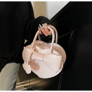 Pink heart-shaped shoulder bag with large bow detail and glossy finish shown held
