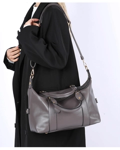 Grey lychee leather pillow bag with gold hardware and adjustable strap on a black coat