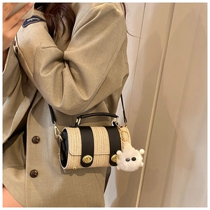 Close-up of straw bucket bag with leather straps, gold clasp, and plush ball charm