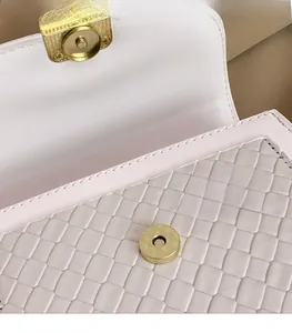 Detail of golden magnetic clasp on a textured woven crossbody flap bag