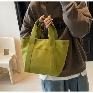 Detail of avocado green canvas tote bag with front pocket and metal rivet accents