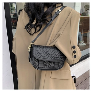 Detail of black woven leather saddle bag with gold metal buckles on a crossbody strap