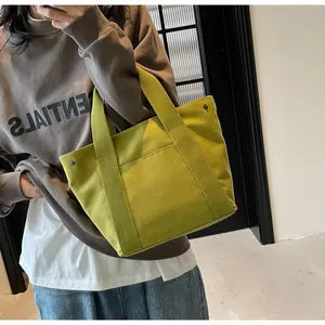 Detail of green canvas tote bag showing reinforced metal rivets and front pocket