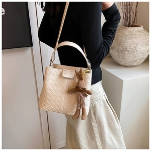 Detail of a beige woven bucket bag featuring a cute bunny plush charm and mini metal buckle