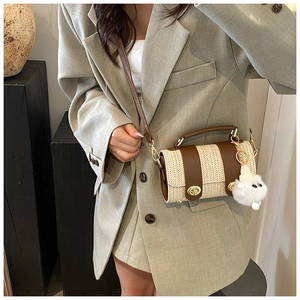 Detail of a beige herringbone cylinder crossbody bag with brown leather straps and pompom