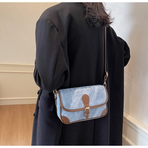 Détail du sac bandoulière en denim bleu avec garniture en similicuir brun et boucle dorée