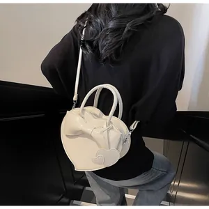 Detail of cream white heart-shaped shoulder bag with bow and dangling heart charms