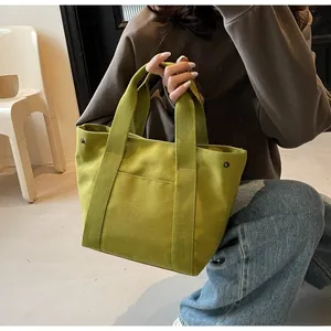 Detail of green canvas tote bag featuring front pocket and metallic rivet studs