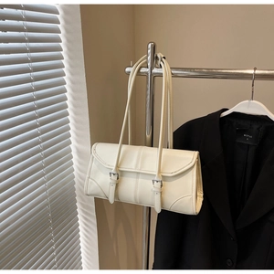 Close-up of cream rectangular shoulder bag featuring parallel buckle straps and glossy finish