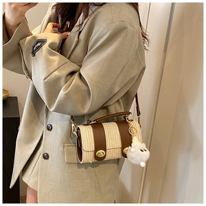 Detail of woven straw cylinder bag with brown leather trim and cute plush pendant