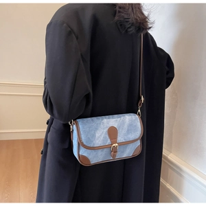 Détail d'un sac bandoulière en denim bleu avec garniture en cuir brun sur manteau noir