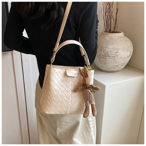 Detail showing creamy white woven bucket bag texture with cute bunny charm and long strap