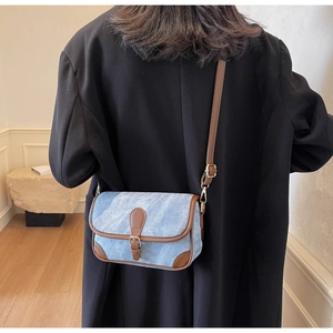 Détail d'un sac bandoulière bleu clair avec bordure en cuir marron porté par un modèle