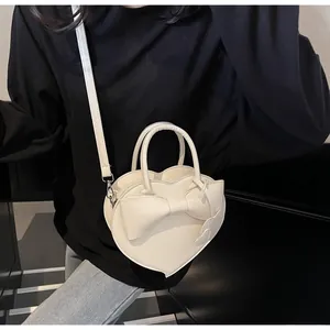 Detail of a heart-shaped cream shoulder bag with a large bow and dual heart charms